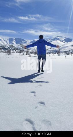 Un uomo con giacca blu che abbraccia la natura innevata e che ha gioia ed essere felicità Foto Stock