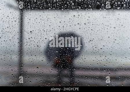 Salvador, Bahia, Brasile - 15 novembre 2021: Un passeggero seduto alla fermata dell'autobus con un ombrello. Salvador, Bahia, Brasile. Foto Stock