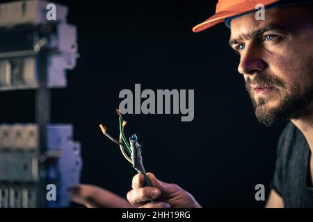 Un elettricista maschio lavora in un quadro elettrico con un cavo di collegamento elettrico. Foto Stock