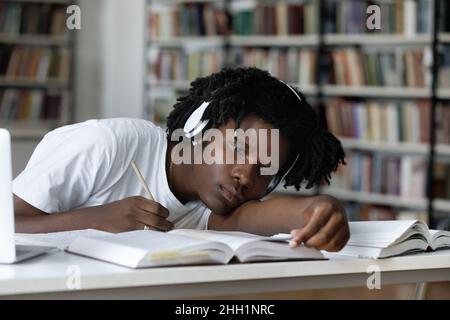 Stanco annoiato pigro studente nero ascoltando la lezione audio Foto Stock