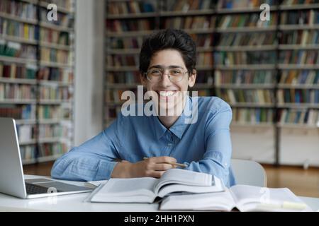 Ragazzo studente fresco felice in occhiali di scrittura saggio in biblioteca Foto Stock