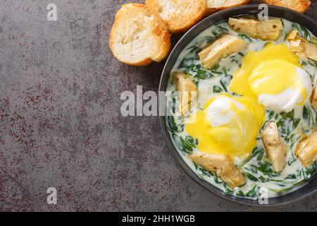 Uova di stile di New Orleans Sardou uova in camicia con carciofo, spinaci e Hollandaise primo piano nel piatto sul tavolo. Vista dall'alto orizzontale Foto Stock