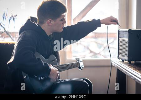 Un giovane suona la chitarra elettrica nella sua stanza. Foto Stock