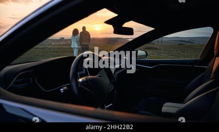 Vista posteriore della giovane coppia in amore godendo la data dell'automobile del tramonto all'ambiente naturale, marito e moglie che trascorrono la sera per unire l'Unione con l'automobile nera per il viaggio che viaggia di fronte Foto Stock