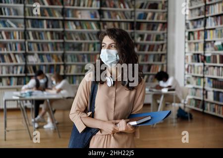 Sorridente ispanica femmina studente in maschera medica protettiva visita pubblico Foto Stock