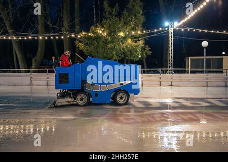 Un operatore dello stadio pulisce una pista di pattinaggio su una moderna macchina per la pulizia del ghiaccio blu. Foto Stock