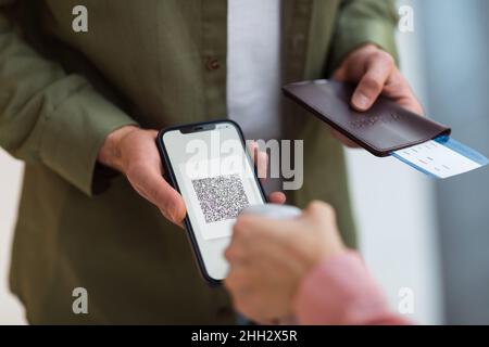 Uomo irriconoscibile che mostra certificato di vaccinazione al telefono in piedi indoor Foto Stock
