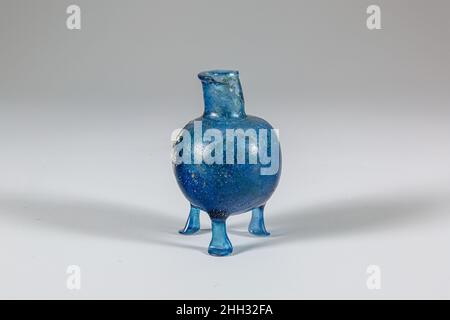 Bottiglia di vetro con tre piedi metà 1st secolo d.C. romana traslucido blu cobalto profondo.bordo pieno con labbro orizzontale rovesciato; collo cilindrico; spalla inclinata; corpo globulare con tre aste piene intorno alla base, tirate e utensili, terminanti in piedi scheggiati e schiacciati; Fondo leggermente arrotondato con indent.Broken irregolare, con grande foro nel bordo e collo e la maggior parte di due gambe mancanti, ma corpo completo; molte bolle di pinprick e striature soffianti; alcuni vaiolatura e una patch di intemperie folte iridescenti su esterno, incrostazione del suolo, intemperie, e iridescenza brillante su interno.. Bott. In vetro Foto Stock
