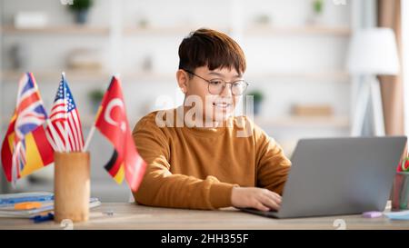 Ragazzo adolescente cinese felice usando il portatile, imparando la lingua straniera in linea Foto Stock