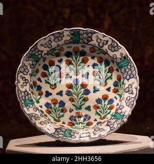 Piatto con pattern di piante fiorite ca. 1565–70 il piatto ha una base appiattita, un bordo piatto e smerlato, e si trova su un anello per il piede. E' decorata con un motivo generale di tulipani disposti in file sfalsate. Tra questi fiori ci sono fintamani o motivi a triplo punto. Sul bordo sono stati dipinti motivi a spirale. Piatto con pattern di piante fiorite. Ca. 1565–70. Stonepaste; policromo verniciato con smalto trasparente. Fabbricato in Turchia, Iznik. Ceramica Foto Stock