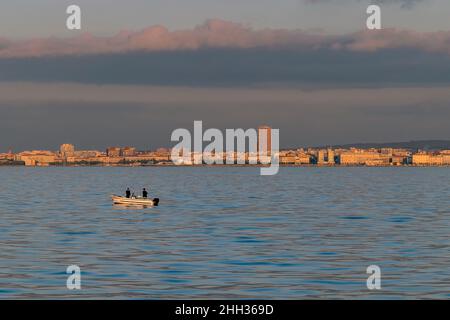 Due pescatori con canne da pesca su un motoscafo al largo della costa di Livorno, Italia, al tramonto Foto Stock