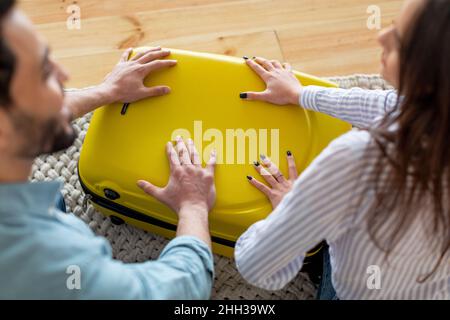 Prepararsi per le vacanze. Mani di uomo e donna che premono sulla valigia, cercando di chiuderla, confezionando abiti per il viaggio Foto Stock