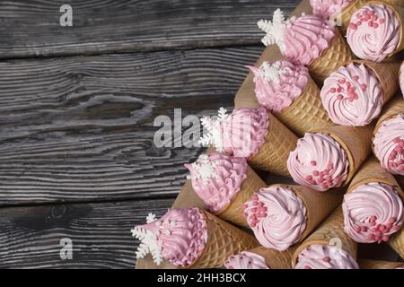 Marshmallow rosa in coni waffle. Zephyr in coni waffle. Decorato con spolverini decorativi e fiocchi di neve mastici. Foto Stock