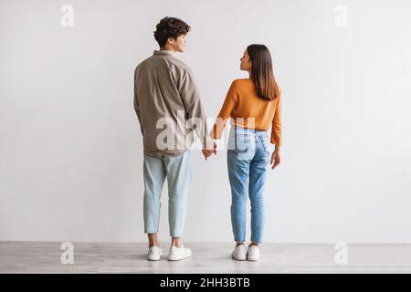Tutta la lunghezza del giovane uomo e della donna asiatici in piedi con le spalle alla macchina fotografica, guardandosi l'un l'altro e tenendo le mani Foto Stock
