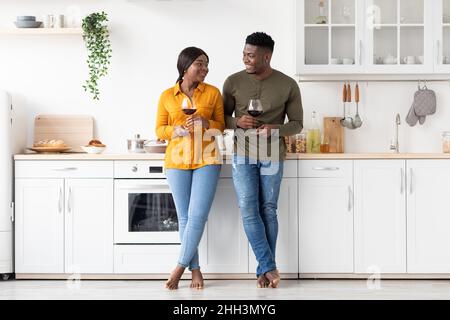 Coppia nera romantica bere vino rosso insieme in cucina, festeggiando San Valentino Foto Stock