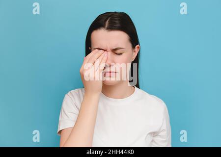 Stanco giovane donna caucasica 20s anni massaggiando ponte nasale, sensazione di affaticamento oculare, signora esausta che soffre di mal di testa o emicrania, isolato sopra Foto Stock