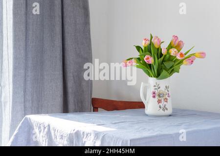 Bel bouquet primaverile di tulipani rosa in una brocca sul tavolo, fiori in un interno casa Foto Stock