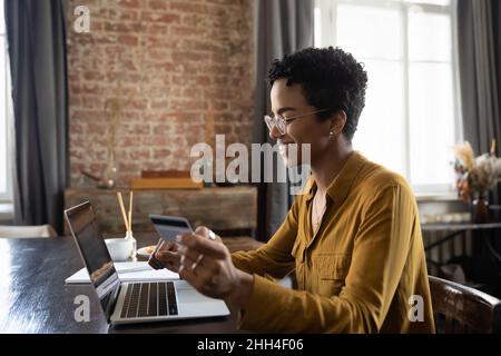 Felice giovane donna che usa il portatile, carta di credito per lo shopping online Foto Stock