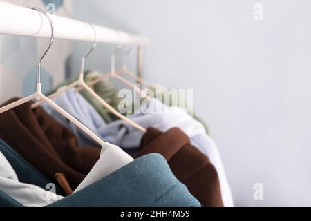 Fila di felpe con cappuccio multicolore in maglia, maglioni sportivi appesi su un appendino in un atelier o abbigliamento sportivo del negozio Retail in primo piano. Colori pastello freddi. Foto Stock