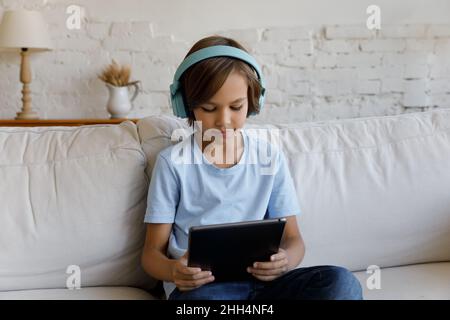 Ragazzo di scuola serio concentrato in cuffie wireless lettura libro Foto Stock