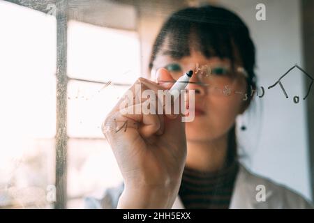 Giovane scienziato che scrive su vetro trasparente in laboratorio Foto Stock