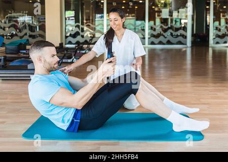 Istruttore di fitness che aiuta lo sportivo a fare pilates esercizio in palestra Foto Stock
