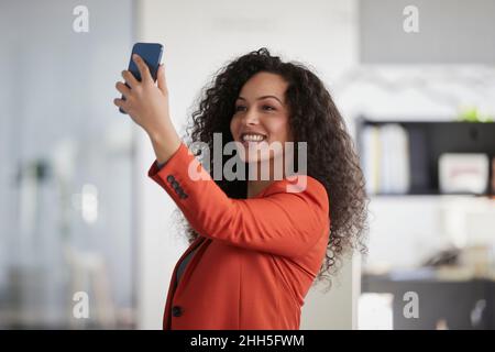 Donna d'affari sorridente che prende il selfie attraverso lo smartphone sul posto di lavoro Foto Stock