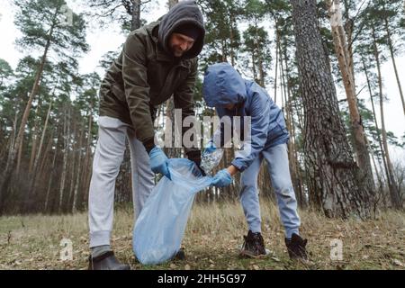 Padre e figlio raccogliendo rifiuti di plastica in sacco di rifiuti a foresta Foto Stock