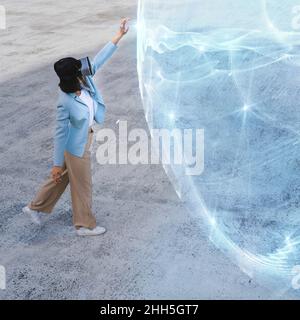 Ragazza adolescente con cuffie per realtà virtuale che toccano la sfera luminosa blu sul sentiero Foto Stock