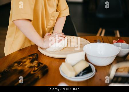Ragazzo impastando la pasta per pizza sul tavolo a casa Foto Stock