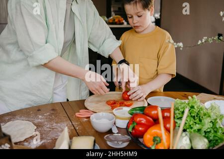 Donna che insegna a tagliare il pomodoro a casa Foto Stock