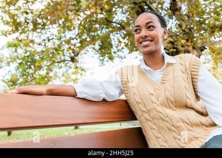 Ragazza sorridente in maglione seduto su panca Foto Stock