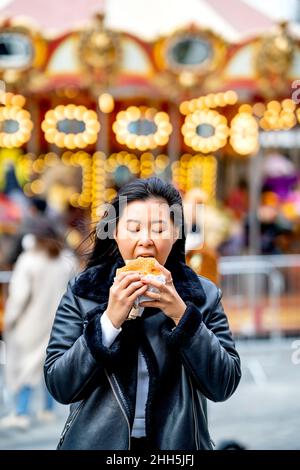 Donna che mangia hamburger al parco divertimenti Foto Stock