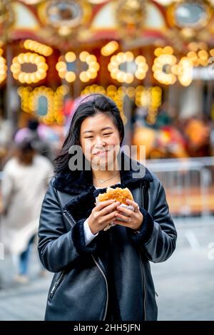 Giovane donna sorridente che tiene hamburger al parco divertimenti Foto Stock