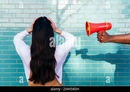 Mano dell'uomo che tiene il megafono dalla donna che ricopre le orecchie davanti al muro turchese Foto Stock