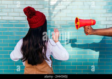 Mano dell'uomo che tiene il megafono dalla donna che gesturing davanti al muro di mattone turchese Foto Stock