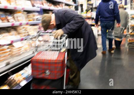 Persona senior con paniere che si piega da scaffali alimentari shopping in M&S Marks e Spencer supermercato negozio Aisle gennaio 2022 Galles UK KATHY DEWITT Foto Stock