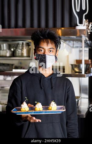 Cameriere con maschera protettiva per il viso con vassoio dessert al ristorante Foto Stock