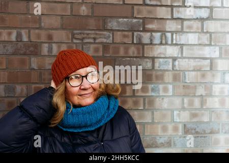 Donna anziana che regola cappello a maglia davanti al muro Foto Stock