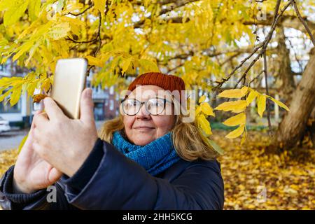 Donna anziana che prende selfie su smartphone nel parco autunnale Foto Stock