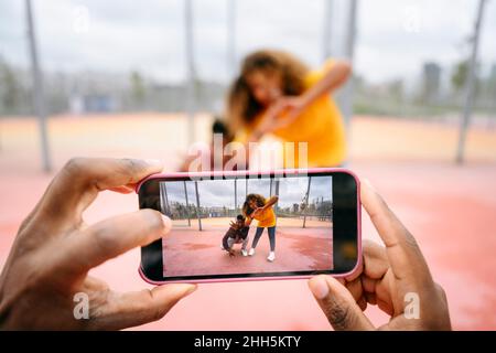 Uomo che fotografa gli amici tramite smartphone presso il campo sportivo Foto Stock