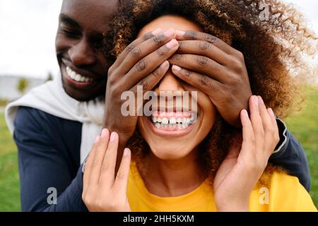 Felice giovane uomo che copre gli occhi dell'amico con le mani al parco Foto Stock
