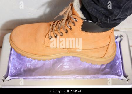 Dispositivo per la ravvivatura automatica di copriscarpe, uomo in scarpe marroni mette su copriscarpe, clintoper meccanico. Foto Stock