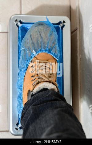 Copriscarpe e un clinthoper, un organizzatore per copriscarpe monouso in ospedale, un uomo mette su scarpe copriscarpe per la pulizia nella stanza, un Foto Stock