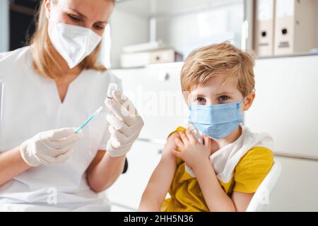 Ragazzo con maschera protettiva per il viso che viene vaccinato al centro Foto Stock