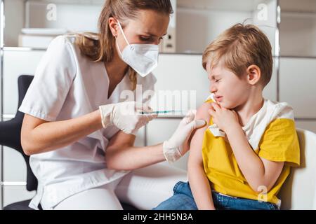 Ragazzo chiudendo gli occhi e farsi vaccinare da infermiera al centro Foto Stock