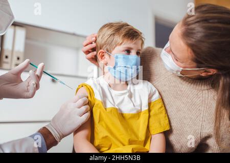 Ragazzo che viene vaccinato dal medico con la madre al centro Foto Stock