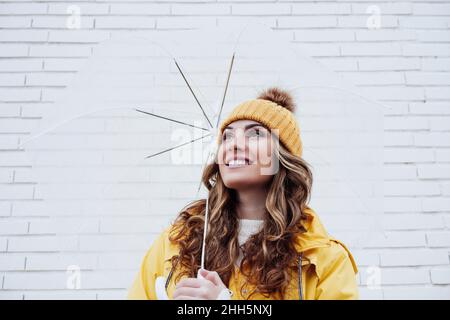 Donna sorridente che tiene l'ombrello davanti al muro Foto Stock