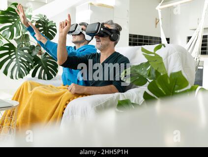 Coppia gay che usa cuffie per realtà virtuale a casa Foto Stock