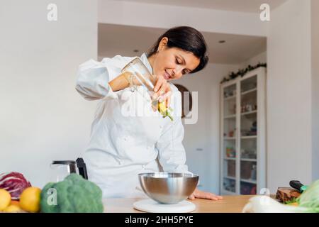 Lo chef sorridente versa l'olio da cucina in una ciotola sul tavolo di casa Foto Stock